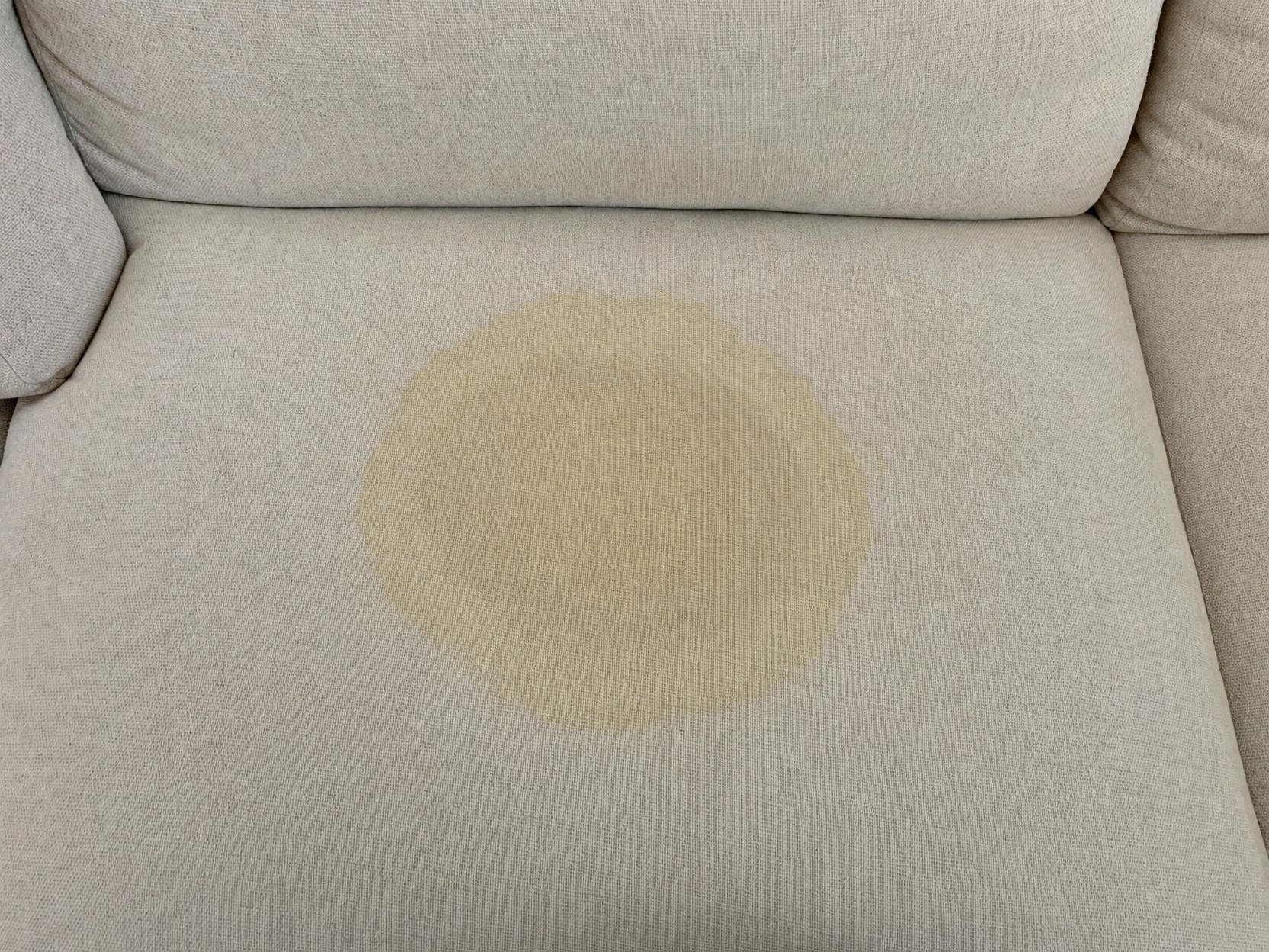 Pernă de canapea textilă cu pată de urină de animal și contur gălbui, înainte de tratamentul cu Urine Stain Remover PRO
